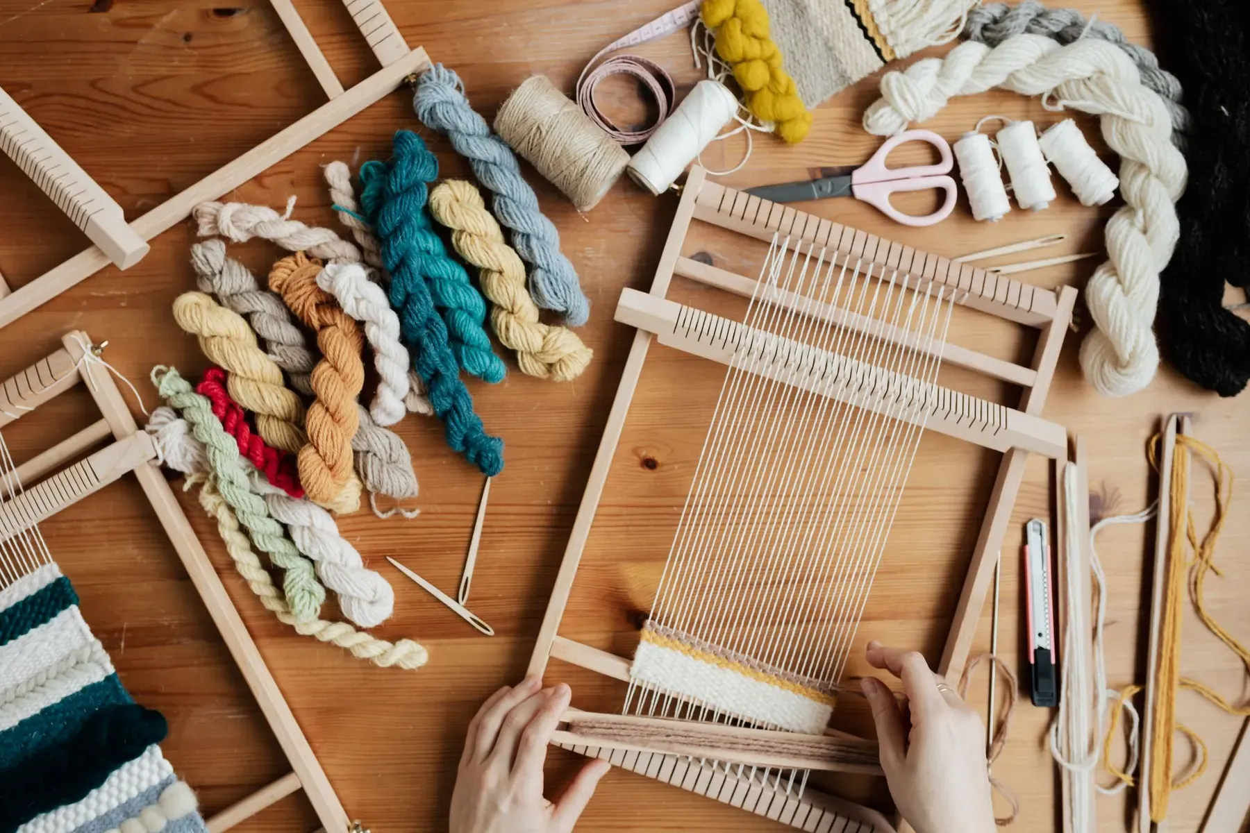 Hands working warp threads on a small wooden loom